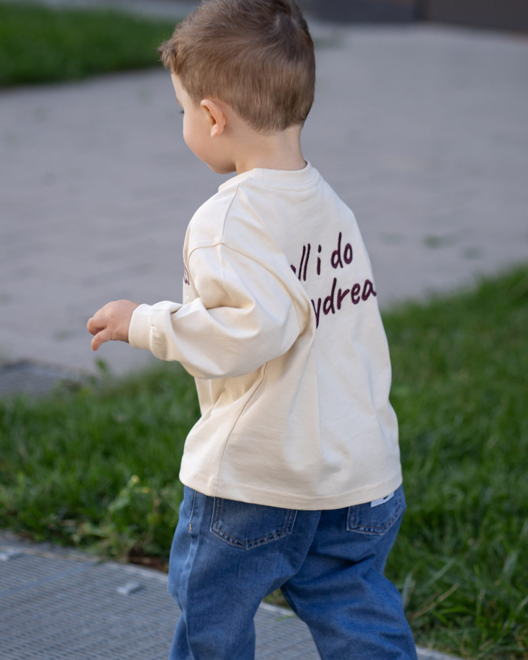 Junge seitlich von hinten in Bewegung, cremefarbenes Daydream Longsleeve und blaue Jeans im oversized Schnitt von Comfy Studios.