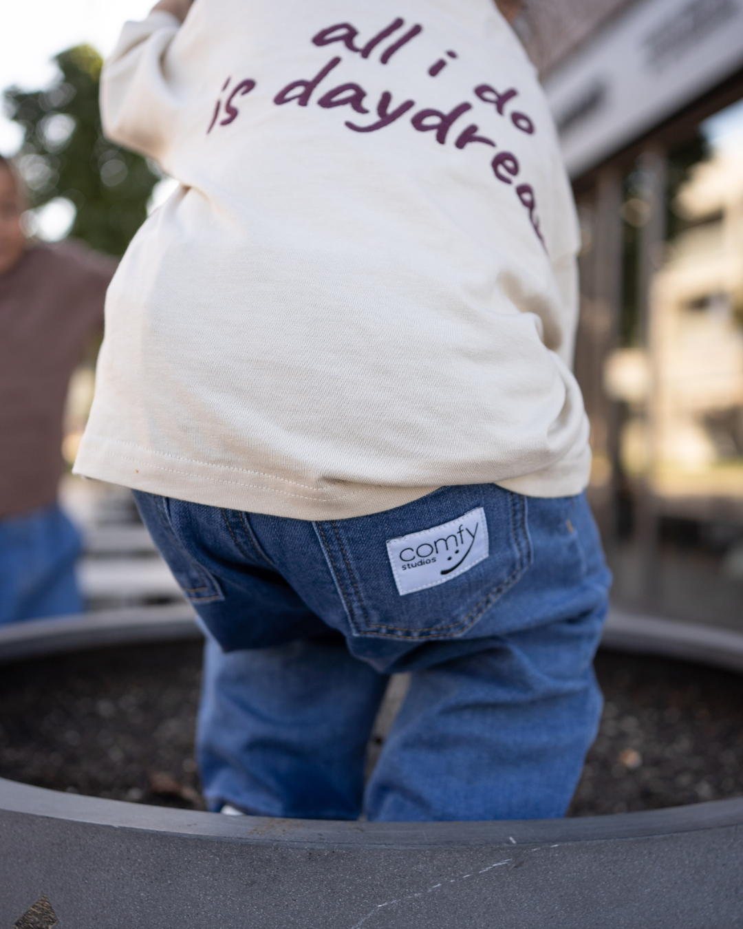 Detail der blauen Oversize-Jeans mit Comfy Studios Label an der Gesäßtasche und dem Saum des cremefarbenen Daydream Longsleeve.