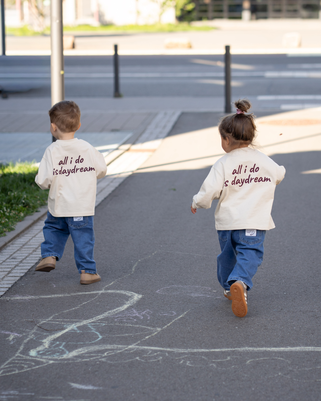 Zwei Kinder in verschiedenen Größen im passenden Daydream Longsleeve mit Rücken-Print und blauer Jeans – Matching-Look von Comfy Studios.