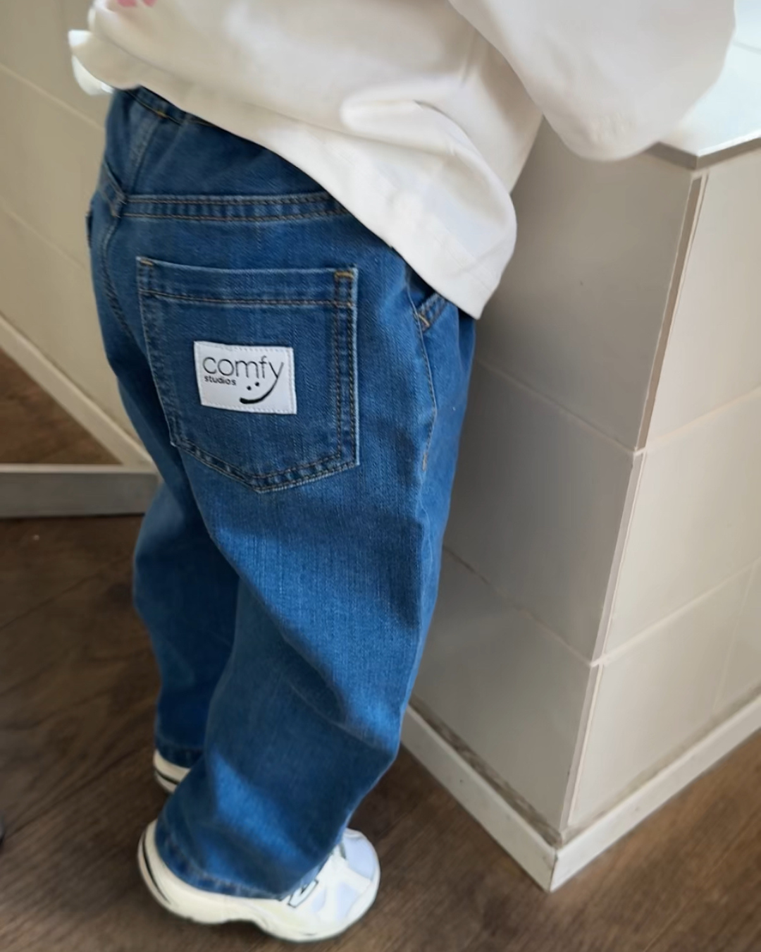 Kind trägt blaue Comfy Studios Jeans mit Kindness Shirt, Comfy Label auf Gesäßtasche sichtbar