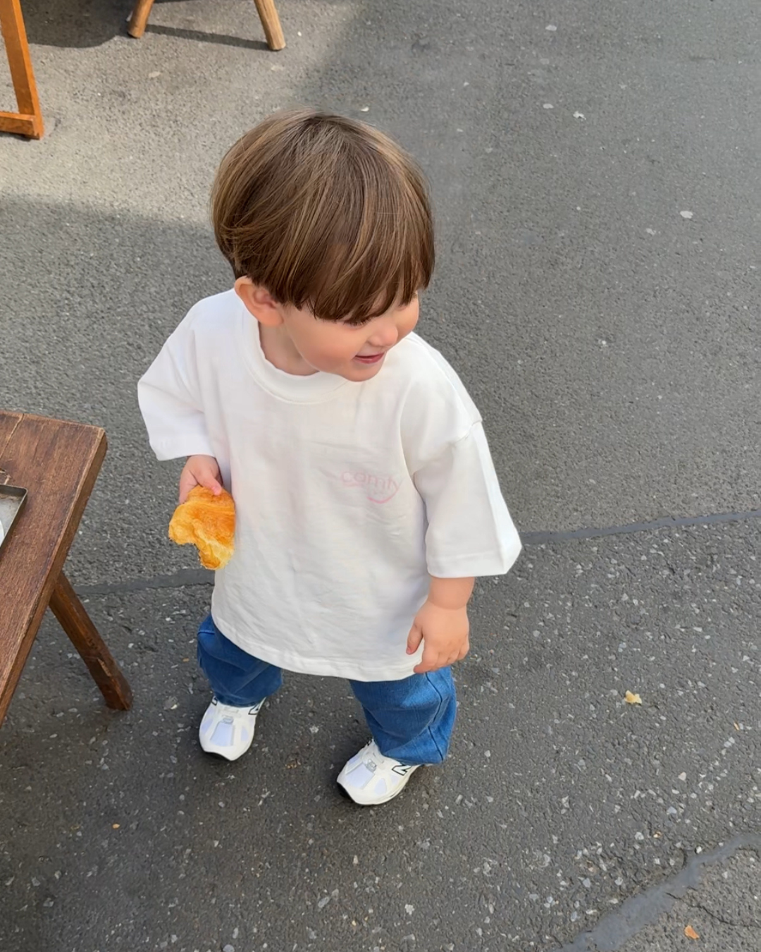 Kleinkind im weißen Kindness Shirt von Comfy Studios, lächelnd auf der Straße – oversize Kinder-T-Shirt mit Jeans kombiniert.