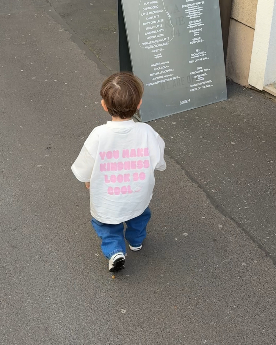 Rückseite des Comfy Studios Kindness Shirts in Rosa mit pinkem Print ‚You make kindness look so cool' auf weißem Oversize-Shirt.