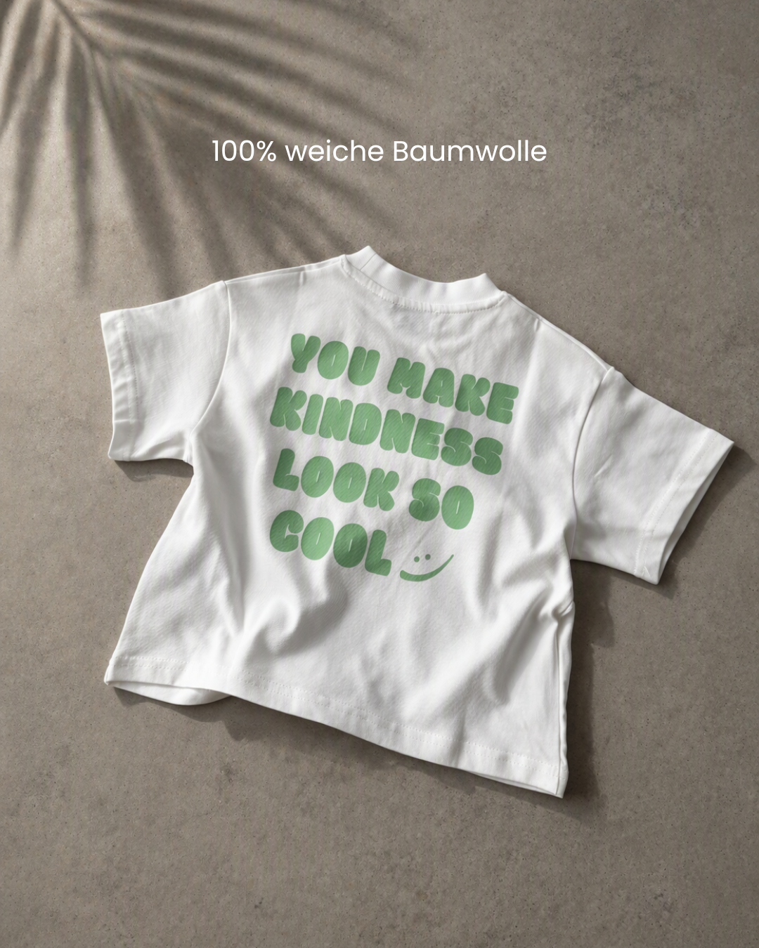 Weißes Kindness Shirt flach auf Beton, Rückenprint sichtbar – Oversize-Schnitt aus 100% Baumwolle.