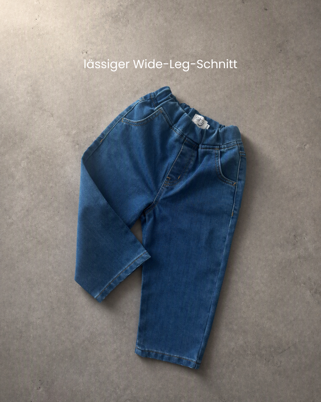 Comfy Studios Kinderjeans blau flach auf Beton, Vorderseite mit Taschen und elastischem Bund