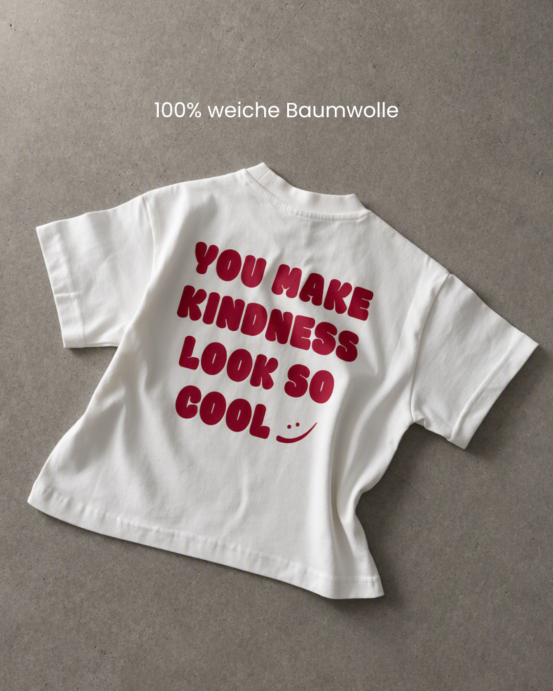 Flat Lay Rückansicht des Kindness Shirts in Weiß mit rotem Print auf Betonhintergrund – 100% weiche Baumwolle