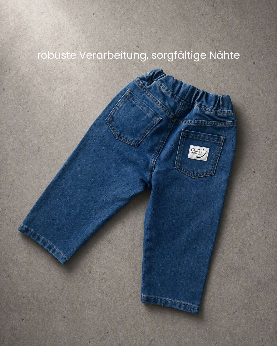 Comfy Studios Kinderjeans blau flach auf Beton, Rückseite mit Comfy Studios Label auf Gesäßtasche