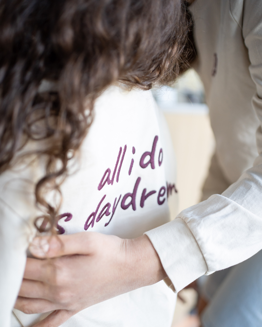 Kind im cremefarbenen Daydream Longsleeve mit Rücken-Print wird von hinten umarmt – warme Szene von Comfy Studios.