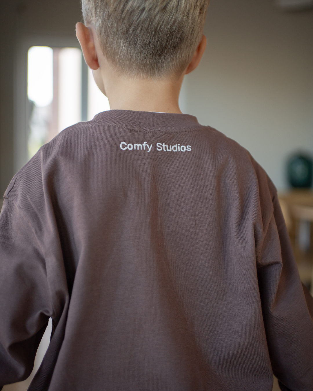 Nahaufnahme des espressobraunen Comfy Studios Longsleeve von hinten mit gestickter „Comfy Studios"-Schrift am oberen Rücken.